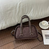 A brown leather mini crossbody bag with a flap and handles resting on a wooden floor next to a white cup.