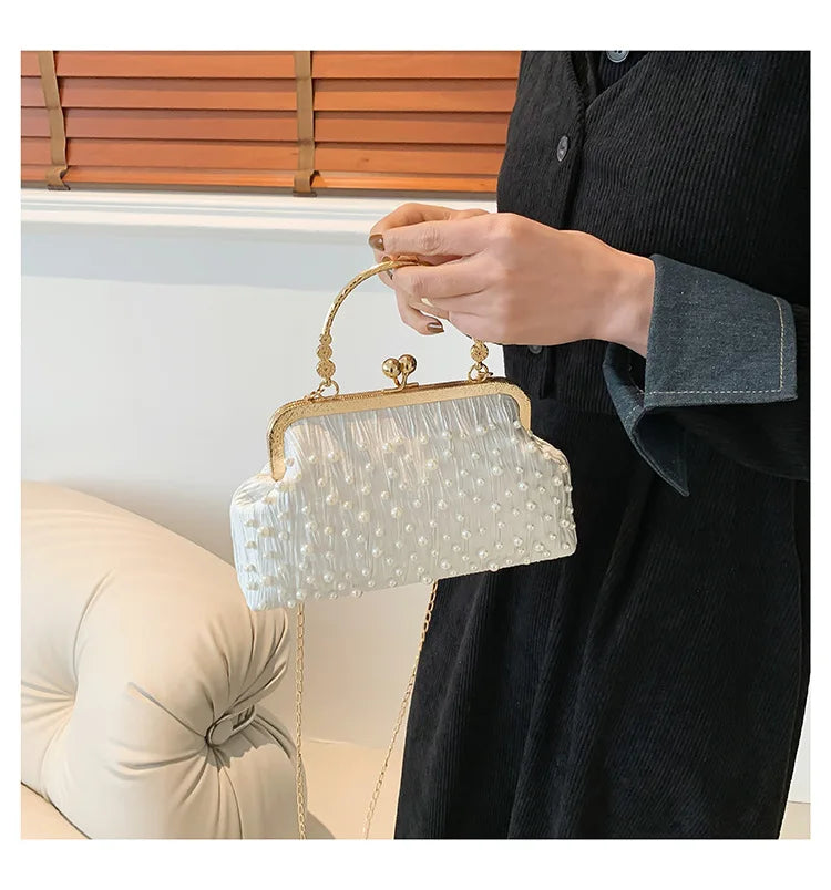 A woman holds a white pearl embellished crossbody shoulder bag against a dark clothing background.