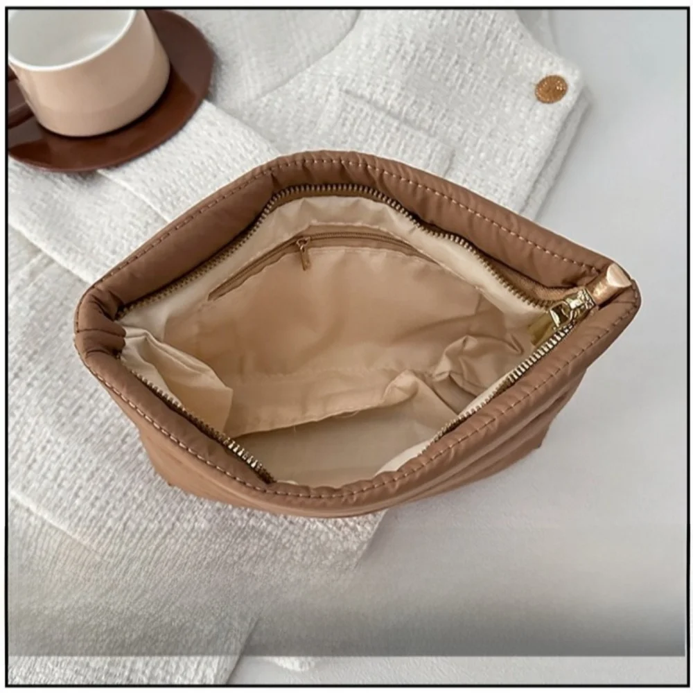 A tan quilted cosmetic travel bag with a gold zipper is shown open on a white textured cloth.