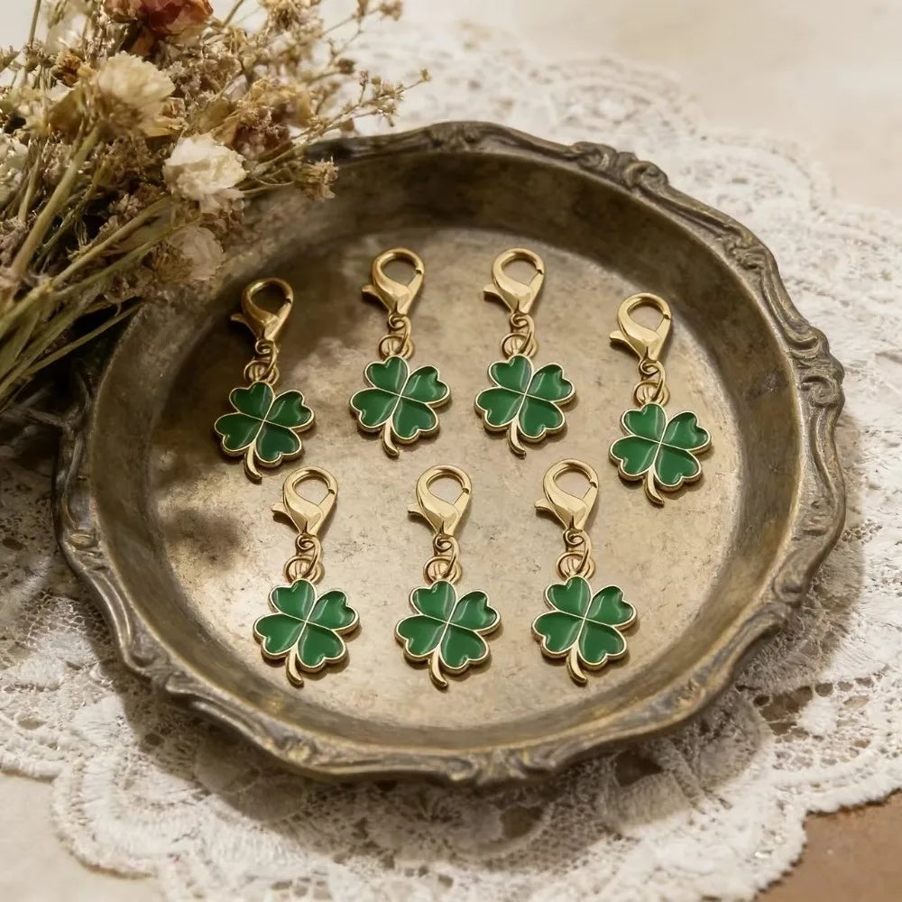 Gold-toned four leaf clover keychains displayed on a silver dish next to dried flowers.