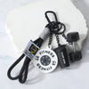 A black detachable dumbbell keychain charm with a fitness disc and a sports bottle attached to a white block.