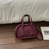 A maroon retro crocodile textured mini crossbody bag resting on a wooden floor next to a white box.