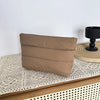 A tan quilted cosmetic travel bag resting on a light woven surface.