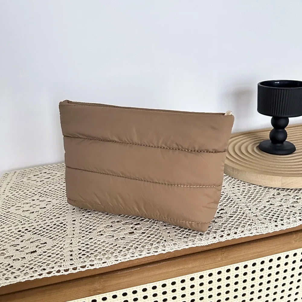 A tan quilted cosmetic travel bag resting on a light woven surface.