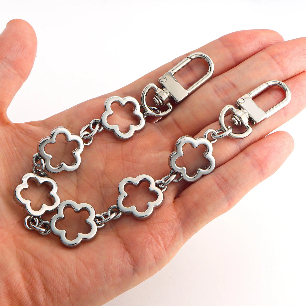Silver flower-shaped extender chain with a clasp shown in a person's hand.