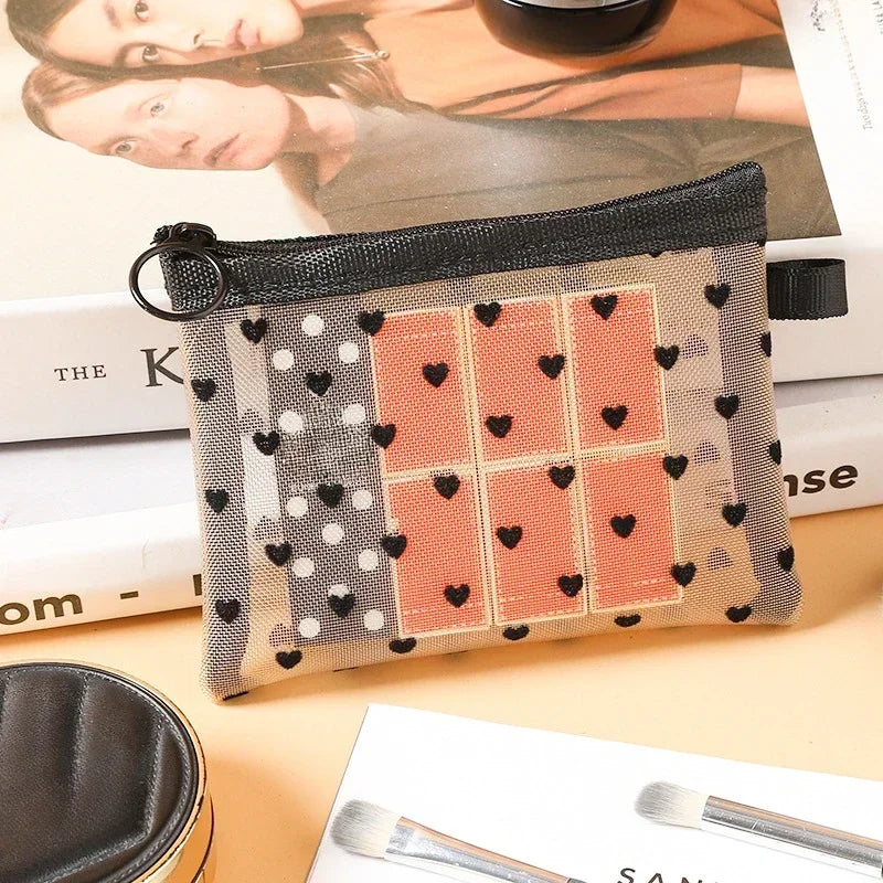 A rectangular mesh cosmetic storage pouch featuring a pattern of pink and gray squares with black hearts.