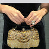 A close-up of a golden diamond rhinestone evening clutch bag with a tassel being held by a person.