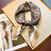 A patterned silk scarf tied in a bow, displayed on a light-colored box next to a magazine photo.