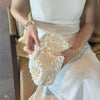 A person holds a white beaded chain shoulder clutch bag in their hands.
