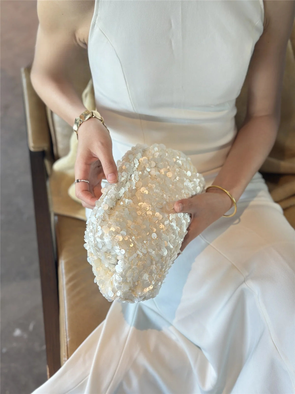 A person holds a white beaded chain shoulder clutch bag in their hands.