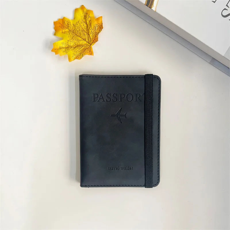 A dark gray passport wallet lies on a white surface next to a yellow autumn leaf.