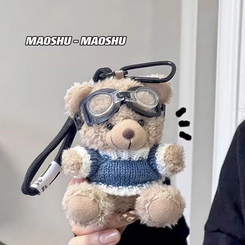 A fluffy brown plush bear keychain wearing a blue knitted sweater and clear glasses.