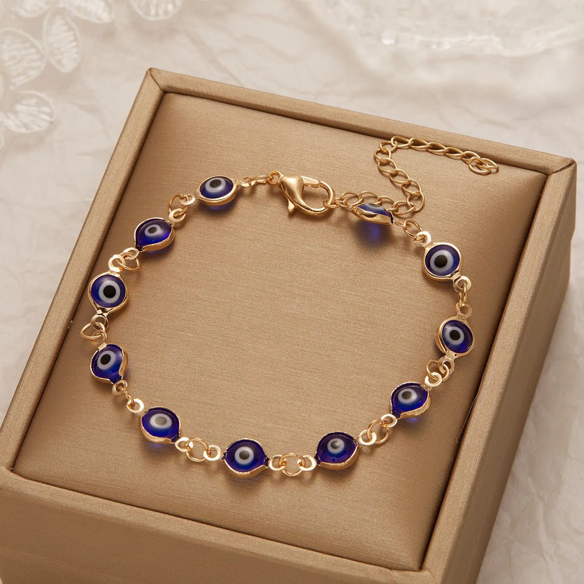 Gold charm bracelet featuring blue evil eye beads on an adjustable chain, presented in a box.