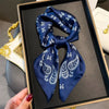 A dark blue paisley silk hair scarf and headband displayed in a wooden frame.