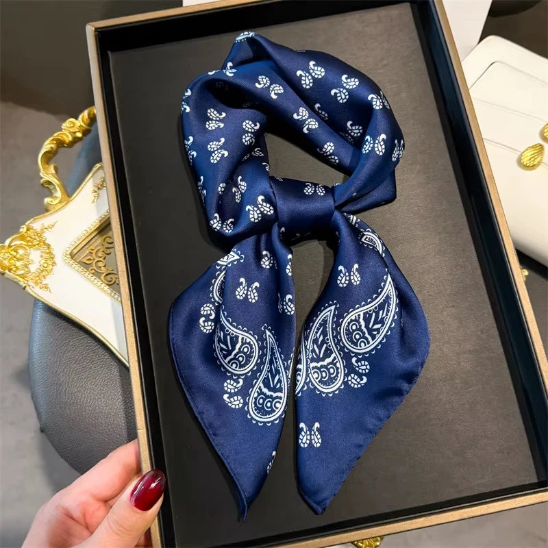 A dark blue paisley silk hair scarf and headband displayed in a wooden frame.