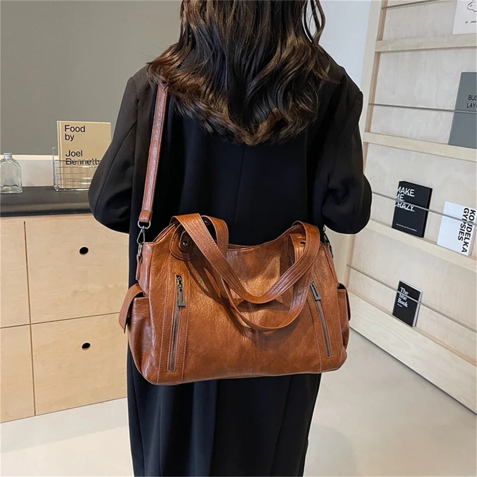 Une femme tient un sac fourre-tout en cuir marron avec plusieurs poches dans un studio.