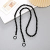 Black acrylic bead cross phone charm necklace laid on a white surface with a light yellow fan in the background
