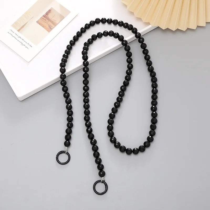 Black acrylic bead cross phone charm necklace laid on a white surface with a light yellow fan in the background