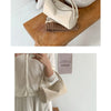 A beige faux suede crossbody bag resting on a wooden surface next to a knitted item.