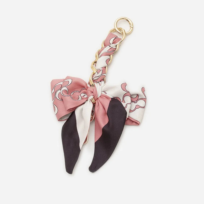 A pink and white patterned fabric bow with a gold chain strap extension for a handbag.