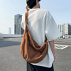 A person wearing a white t-shirt and dark pants is holding a brown corduroy casual crossbody shoulder bag.
