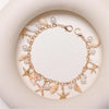 A gold-toned bohemian layered bag chain featuring pearls, seashells, and starfish charms displayed on a light background.