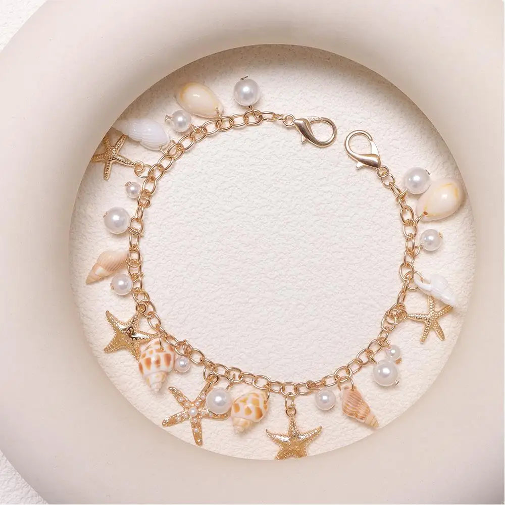 A gold-toned bohemian layered bag chain featuring pearls, seashells, and starfish charms displayed on a light background.