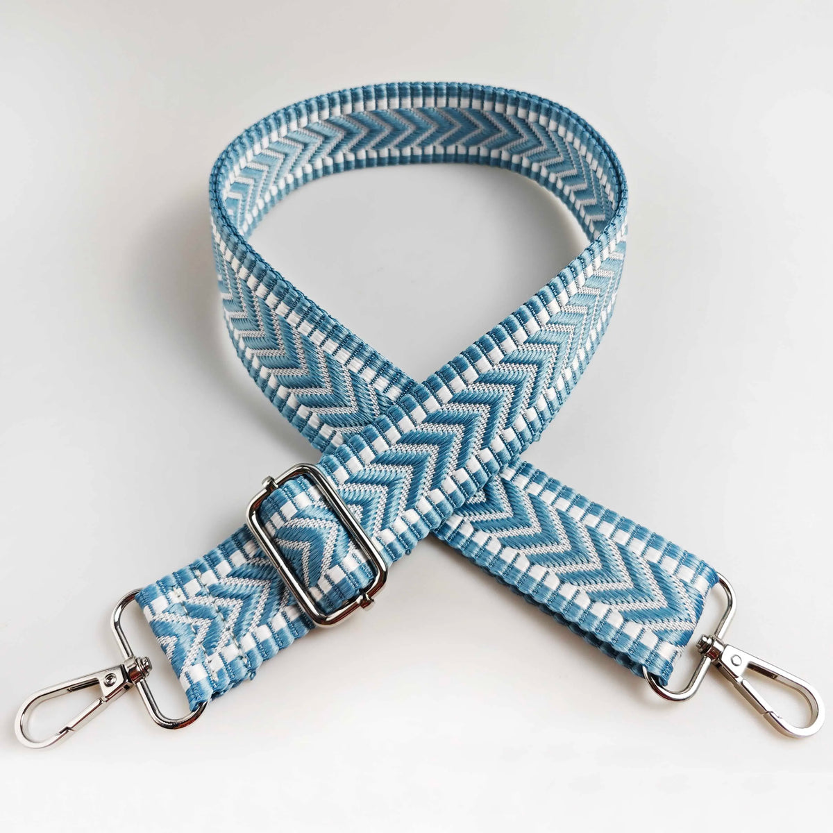A light blue and white woven strap with an arrow jacquard pattern, featuring a silver buckle and metal clasps.