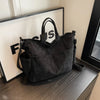 A black corduroy multi-pocket tote bag is displayed on a dark surface next to a framed sign.