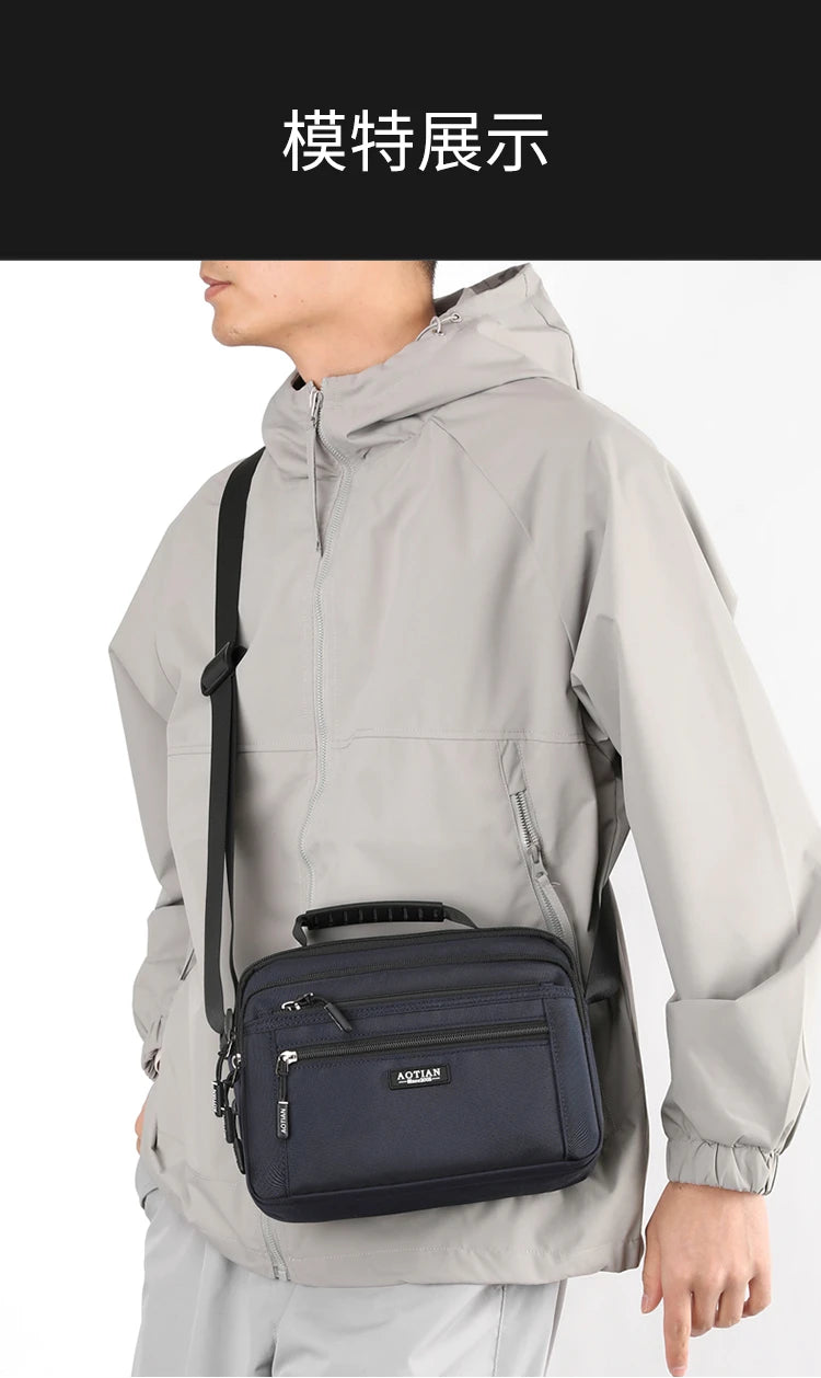 A man wearing a light gray waterproof jacket is holding a navy blue compact crossbody messenger bag.