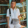 A woman models a white shirt and shorts while carrying a black and white checkered multi-functional waist bag.