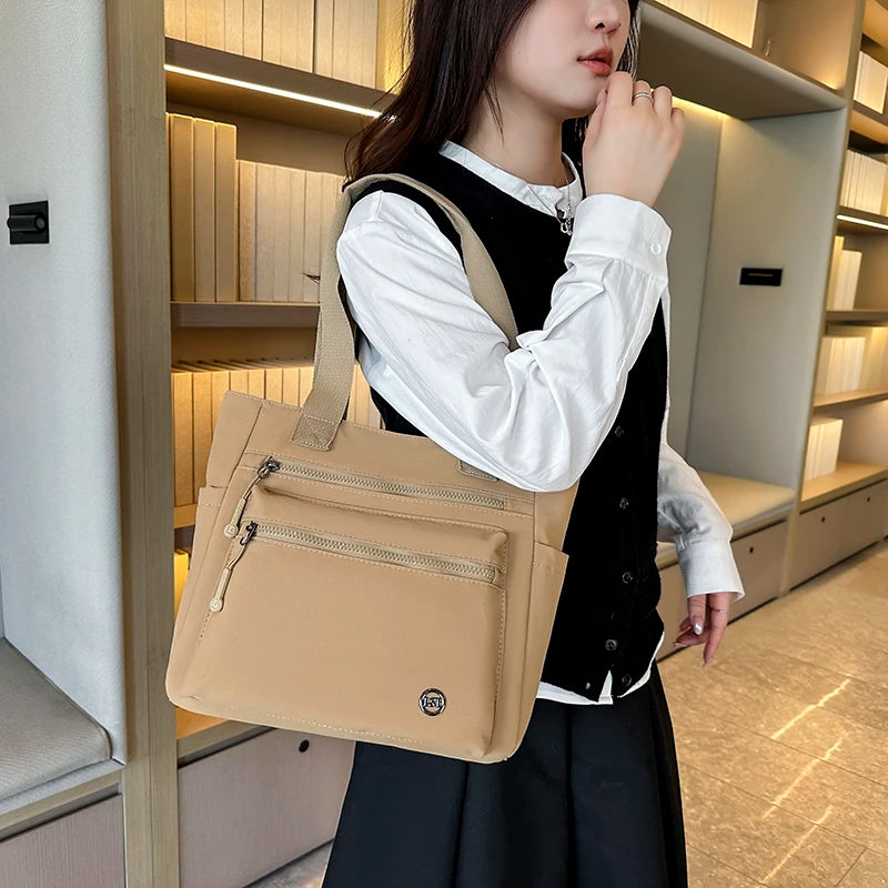 A woman holds a beige canvas tote bag in front of a light wood bookshelf interior.