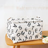 A white fabric storage basket with black letters is shown on a wooden surface.