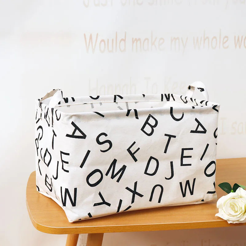 A white fabric storage basket with black letters is shown on a wooden surface.