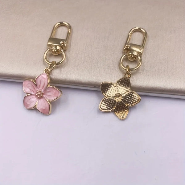 A pair of gold-toned keychains featuring pink and gold resin flowers.