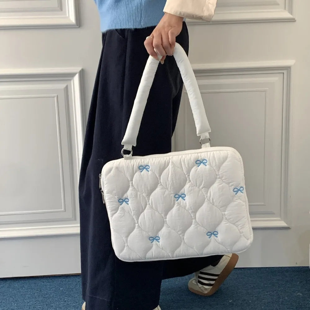 Una mujer sostiene un bolso de ordenador portátil acolchado blanco con detalles de lazo azul.
