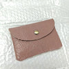 A light pink genuine leather card holder and coin purse with a round gold-toned stud closure.