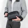 A man holds a black PU leather clutch handbag with a checkered pattern against a gray jacket.