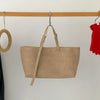 Un sac à main en cuir PU beige et décontracté est suspendu sur un support en bois contre un mur blanc.