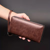 A hand holds a brown PU leather zipper wallet with a stitched edge against a dark background.