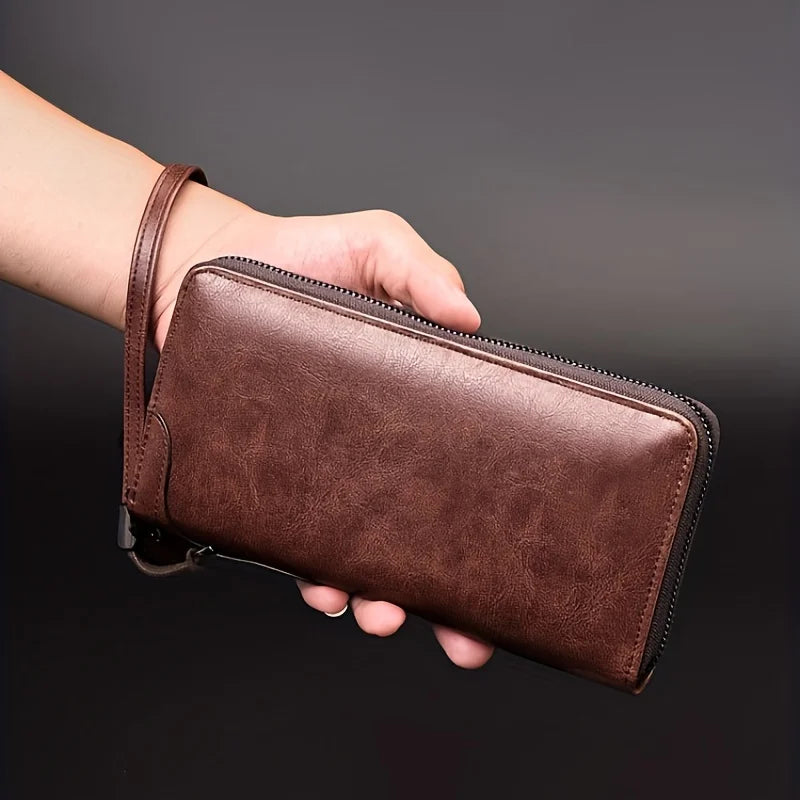 A hand holds a brown PU leather zipper wallet with a stitched edge against a dark background.