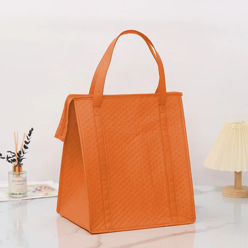 An orange insulated tote bag with a handle is displayed on a white marble surface.
