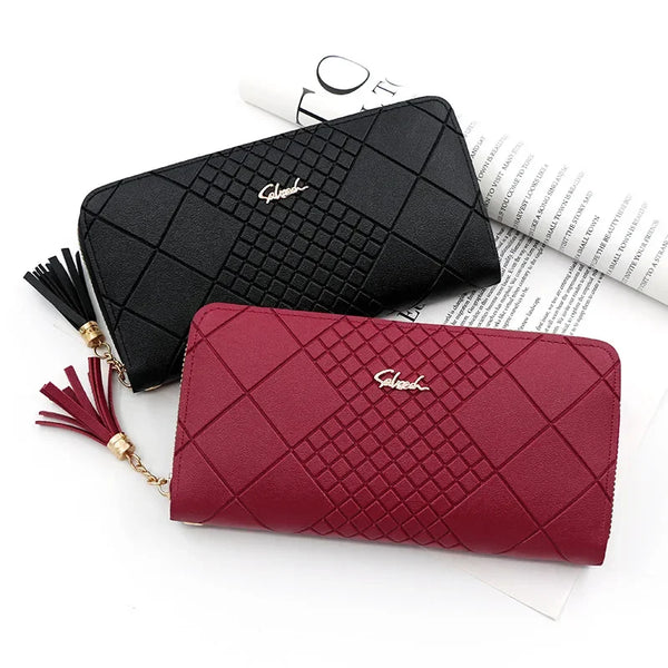 A deep red quilted clutch wallet with gold chain detail resting on a white background next to some paper.