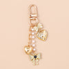 Gold-toned pearl bow heart keychain with a clasp and dangling charms