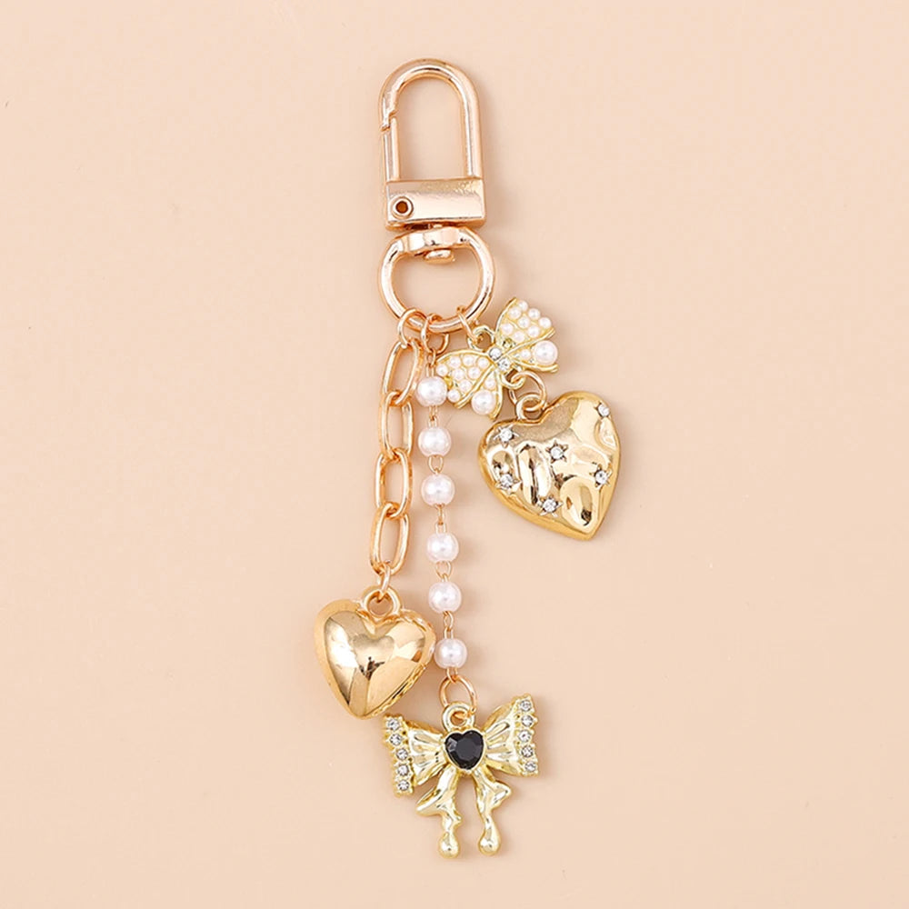 Gold-toned pearl bow heart keychain with a clasp and dangling charms