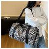 Una mujer sostiene una bolsa de viaje tipo duffel con estampado de leopardo y correa negra y compartimento para zapatos.