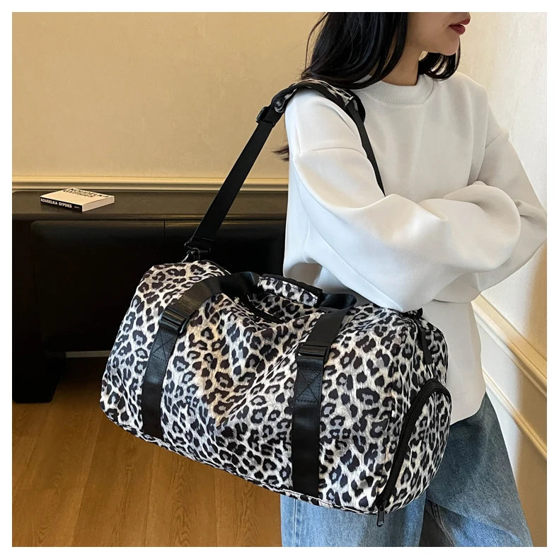 Una mujer sostiene una bolsa de viaje tipo duffel con estampado de leopardo y correa negra y compartimento para zapatos.