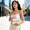 A woman models an elegant cream leather tote bag with gold hardware against a city street backdrop.