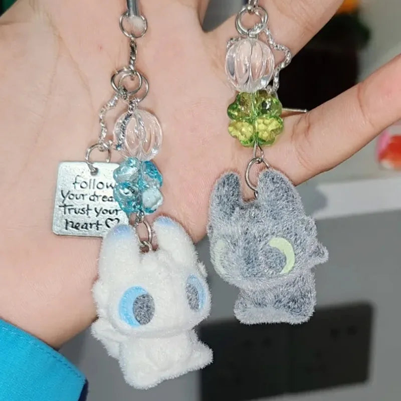 A silver keychain pendant featuring a white cartoon bunny charm with blue eyes and a green bead cluster.