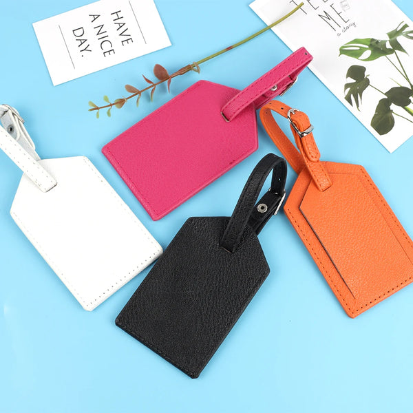 A collection of pink, black, and orange PU leather luggage tags lying on a light blue surface.
